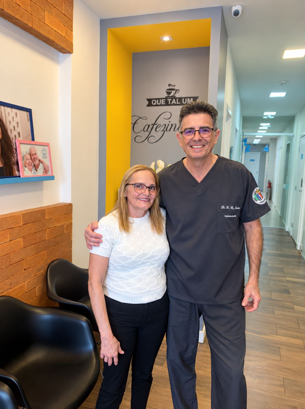 Maria ao lado do Dr. Hugo Robertson na Odontoclinic Vila Mariana após a reabilitação com prótese protocolo superior e inferior